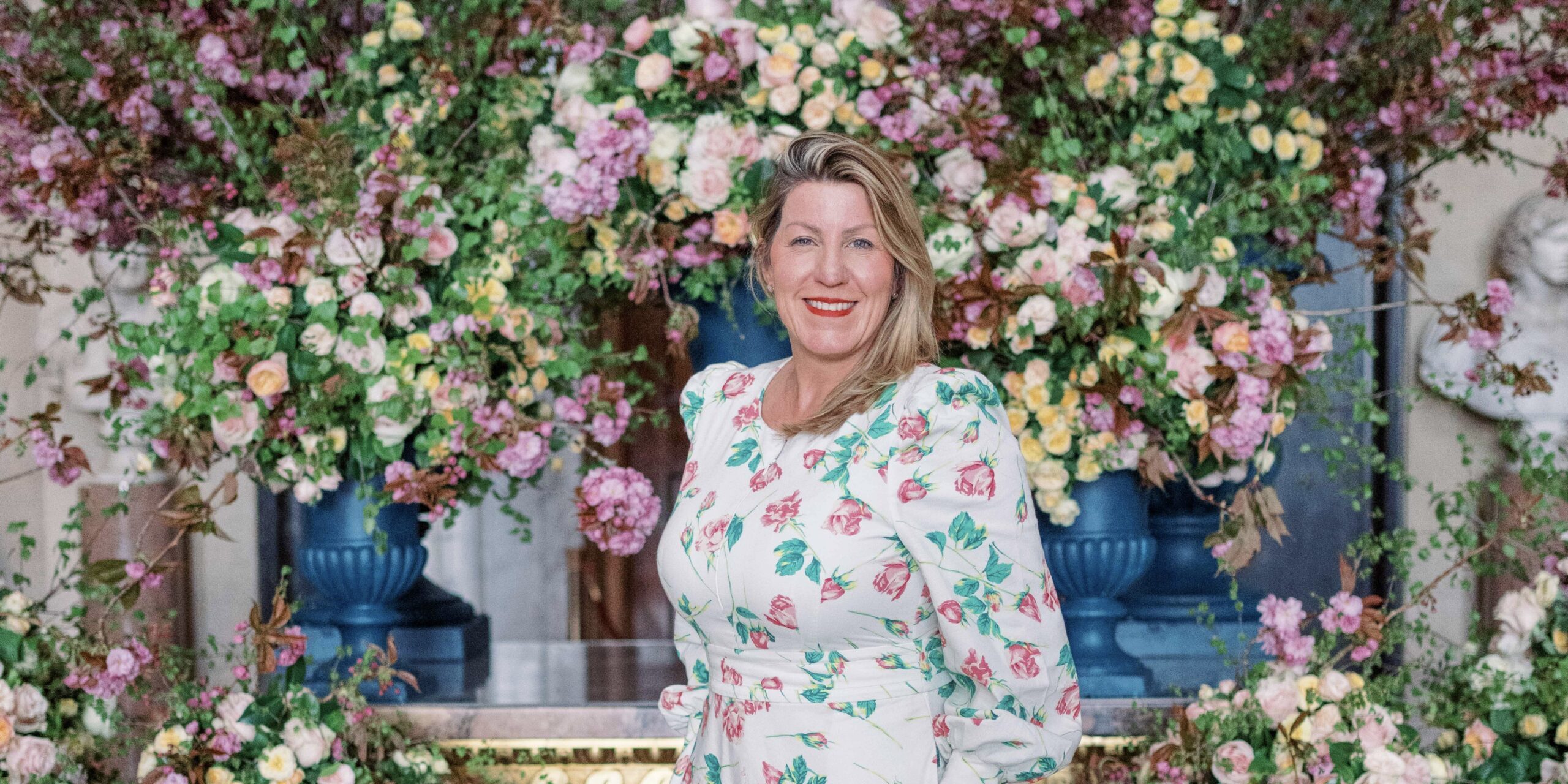 Luxury wedding and events florist and floral mentor, Paula Rooney, wearing a white dress standing in front of a colourful floral installation